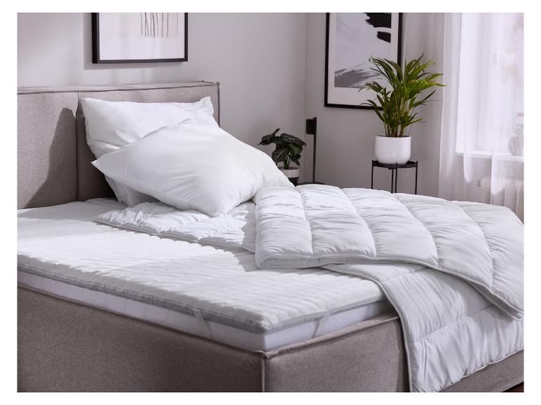 Lit avec couettes blanches, oreillers et surmatelas dans une chambre.