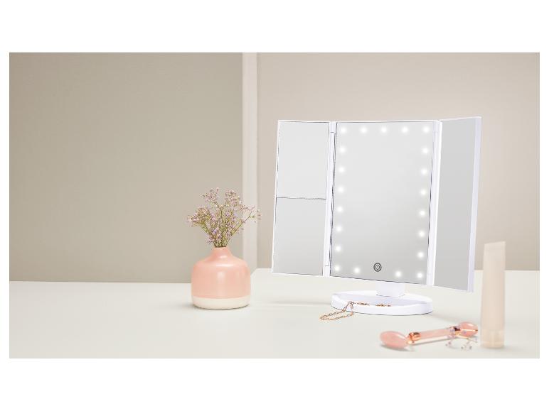 Miroir de maquillage triptyque avec éclairage LED, vase de fleurs et produits de beauté sur une table.