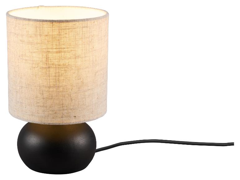 Lampe de table avec base sphérique noire et abat-jour cylindrique en tissu beige, allumée.