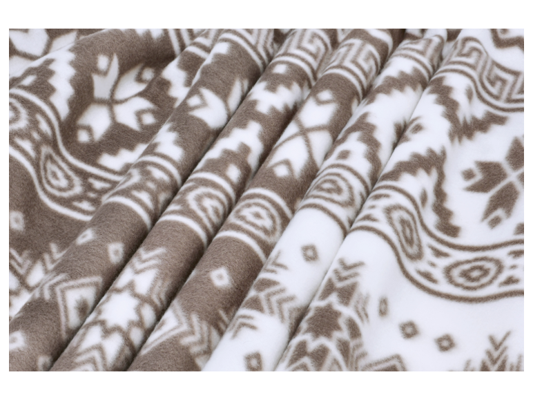 Gros plan sur une couverture en polaire douce avec un motif norvégien marron et blanc.