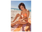 Une femme en bikini mange une orange sur la plage.