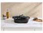 Plat de cuisson rectangulaire noir avec couvercle en verre sur un comptoir de cuisine blanc avec épices et huile.