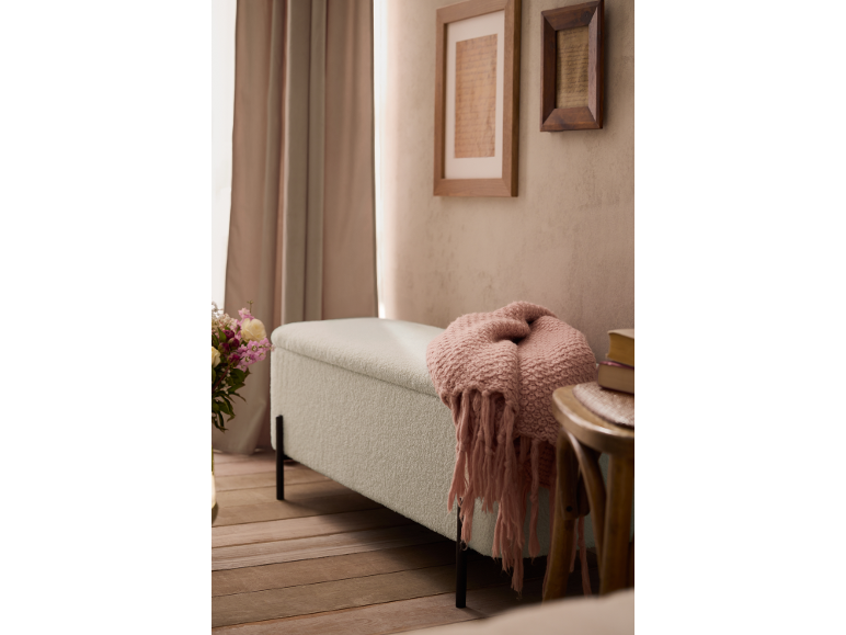 Banc rembourré avec jeté rose, cadres au mur et rideaux dans une pièce.