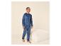 Homme en pyjama velours bleu, debout à côté d'un pouf beige.