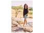 Une femme portant un top noir, un short en jean bleu et des espadrilles blanches.