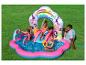 Piscine gonflable thème princesse avec toboggan et arroseur, trois enfants jouent et un père est assis à côté.