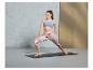 Une femme fait du yoga sur un tapis, vêtue d'un soutien-gorge de sport et de leggings.