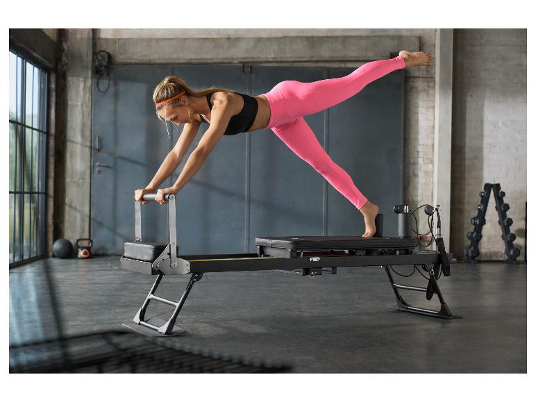 Femme faisant du pilates sur un reformer noir dans une salle de sport.