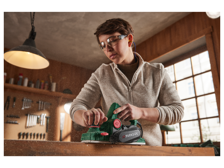 Une femme utilise une raboteuse Parkside pour travailler le bois dans son atelier.