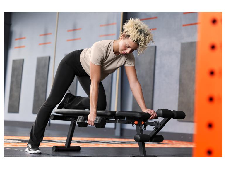 Femme faisant des tirages haltères sur un banc de musculation en salle