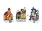 Trois maisons de village de Noël festives avec des toits enneigés, dont une église et un magasin de jouets.