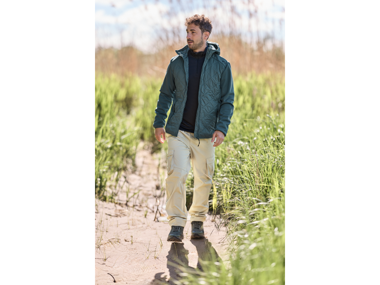 Homme en veste matelassée et pantalon cargo beige marchant sur un chemin de sable.