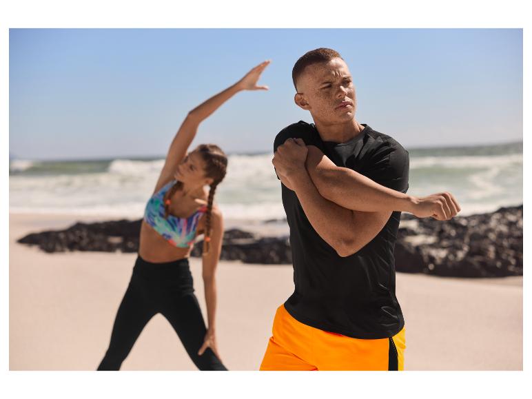 Homme et femme en vêtements de sport s'étirant sur la plage.