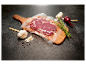 Un steak sous vide sur une planche en bois, avec de l'ail, un oignon et du romarin.