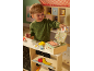 Enfant jouant avec des jouets en bois, dont une caisse enregistreuse et des aliments.