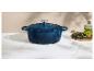 Cocotte en fonte bleue sur un comptoir en marbre avec des herbes et de l'huile d'olive.
