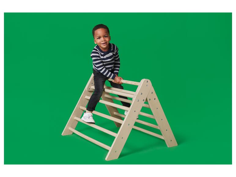 Un garçon heureux grimpe sur une structure d'escalade triangulaire en bois.