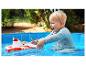Enfant blond jouant avec un bateau de pompiers rouge et blanc dans une piscine bleue.