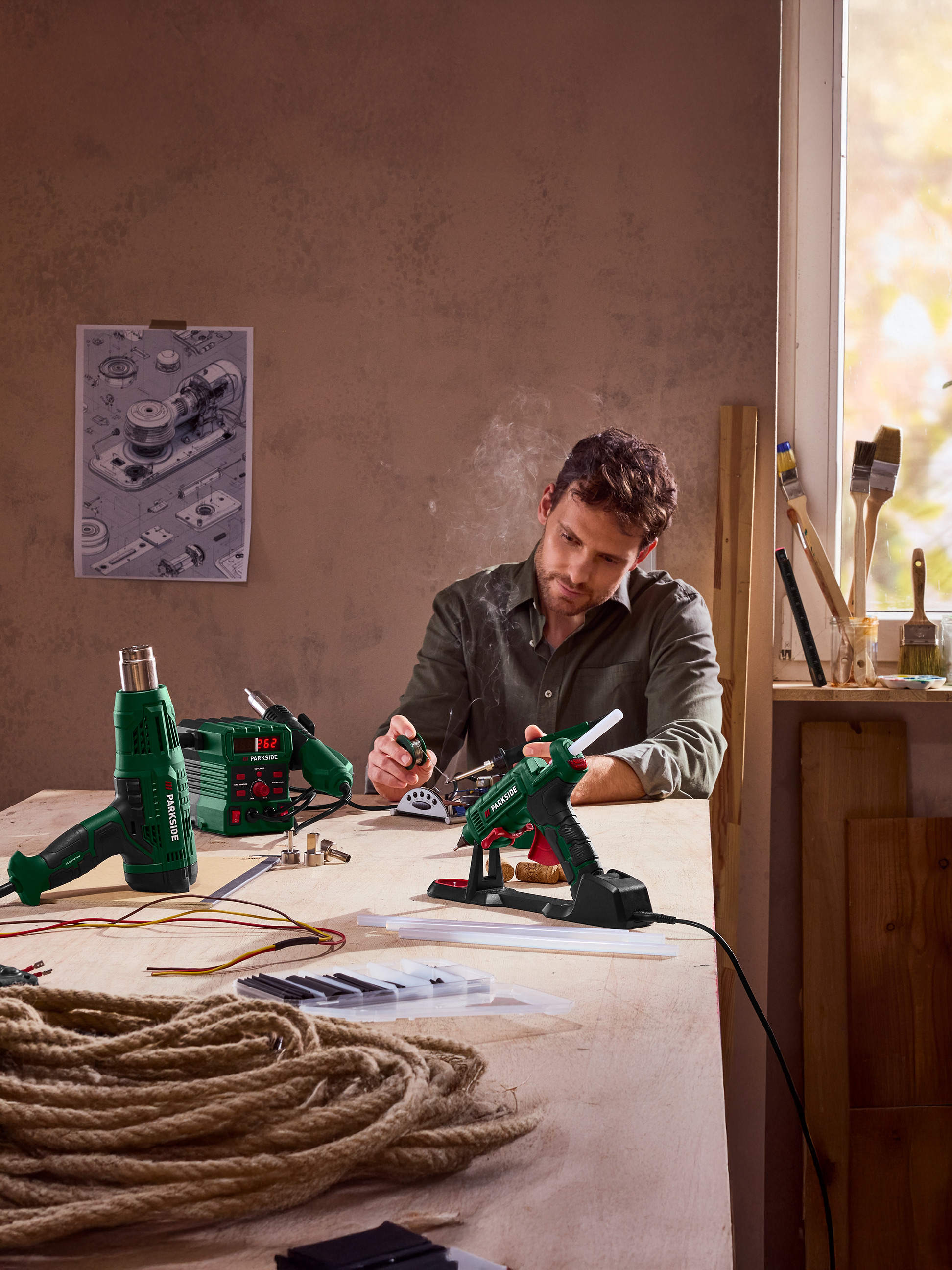 Un homme utilise un pistolet à colle, avec un pistolet thermique et un fer à souder sur la table.