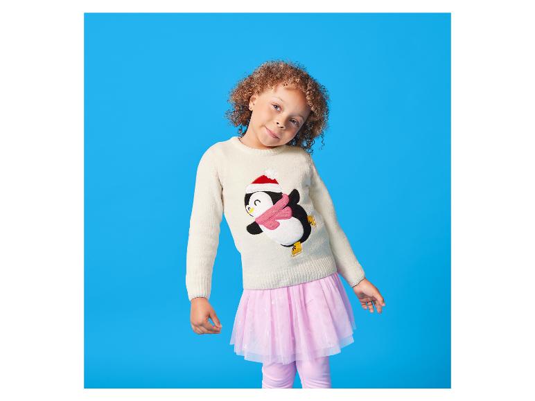 Fillette aux cheveux bouclés portant un pull pingouin et une jupe tutu rose.