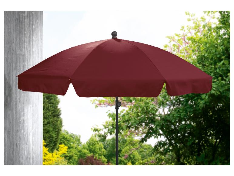 Un parasol rouge dans un jardin avec des arbres verts.