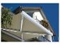 Store banne beige avec éclairage LED au-dessus d'un balcon fleuri sous un ciel bleu.
