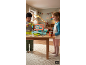 Des enfants jouent avec une caisse enregistreuse en jouet sur une table en bois.