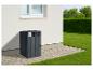 Conteneur à déchets gris foncé à côté d'un mur de maison avec pelouse et buissons.
