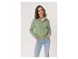 Femme en veste zippée verte et jean, les mains dans les poches.