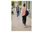 Une femme portant une veste rose avec un motif papillon marche dans la rue avec un sac à dos.