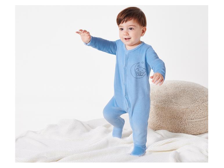 Un bébé vêtu d'une combinaison bleue avec un imprimé d'éléphant se tient sur une couverture blanche.