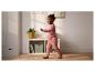 Enfant en tenue rose marchant dans une pièce avec une étagère et une plante.