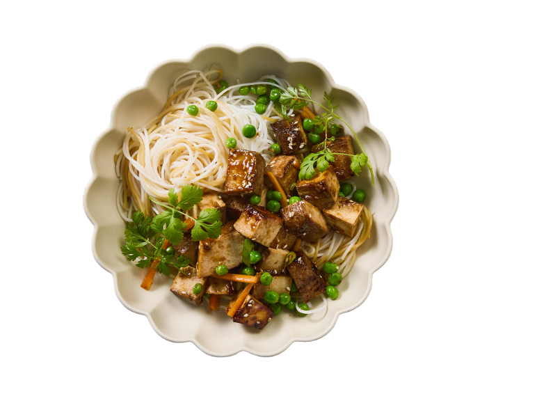 Bol de nouilles de riz, tofu glacé, petits pois et carottes, garni de graines de sésame et de coriandre.