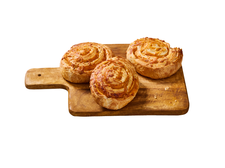 Trois escargots feuilletés au fromage sur une planche à découper en bois.