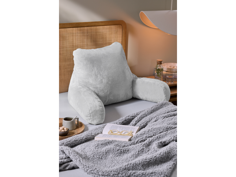 Coussin de lecture gris clair avec accoudoirs sur un lit avec un plaid et un livre.