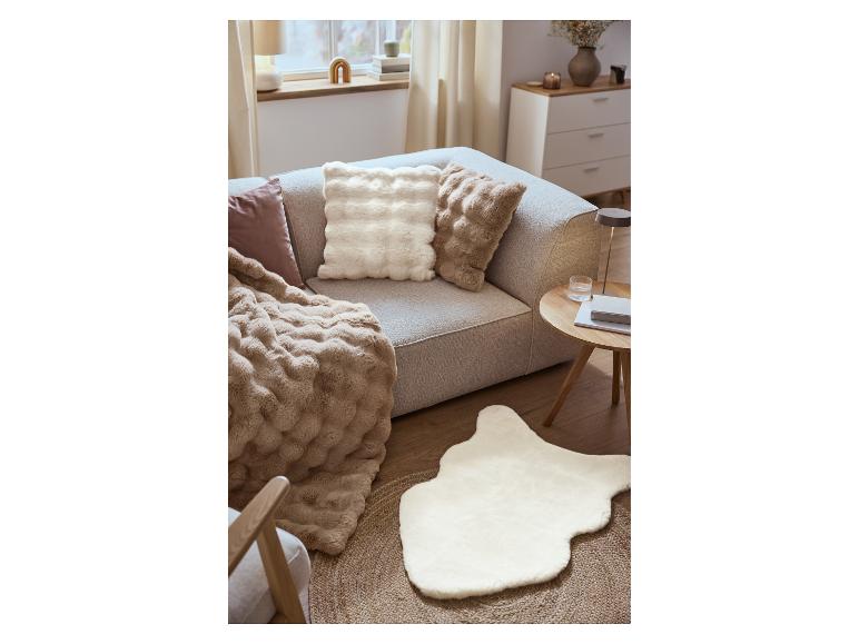 Un canapé gris avec des coussins moelleux et une couverture douce, à côté d'une table basse et d'un tapis en fausse fourrure.