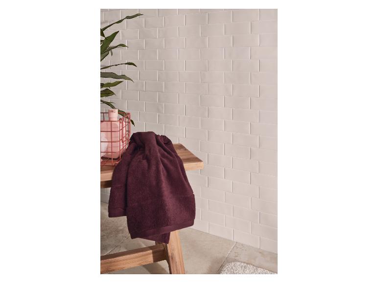 Serviettes de bain sur un banc en bois, avec des murs carrelés et une plante.