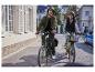 Deux personnes font du vélo électrique, un vert et un beige, en ville.