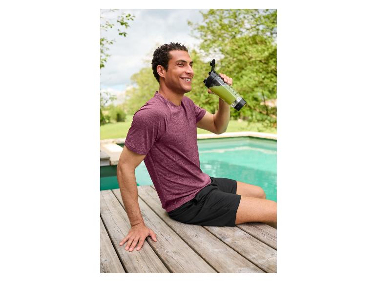 Un homme en t-shirt technique CRIVIT est assis au bord de la piscine et boit un shake vert.