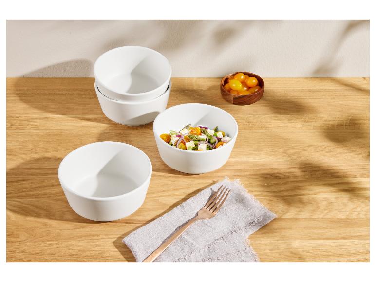 Bol en céramique blanc avec salade, bols empilés et tomates cerises dans un bol en bois.
