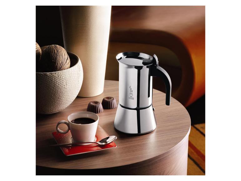 Cafetière moka argentée, tasse de café et chocolats sur une table en bois.