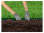 Des mains gantées travaillent la terre avec une bordure verte le long de l'herbe