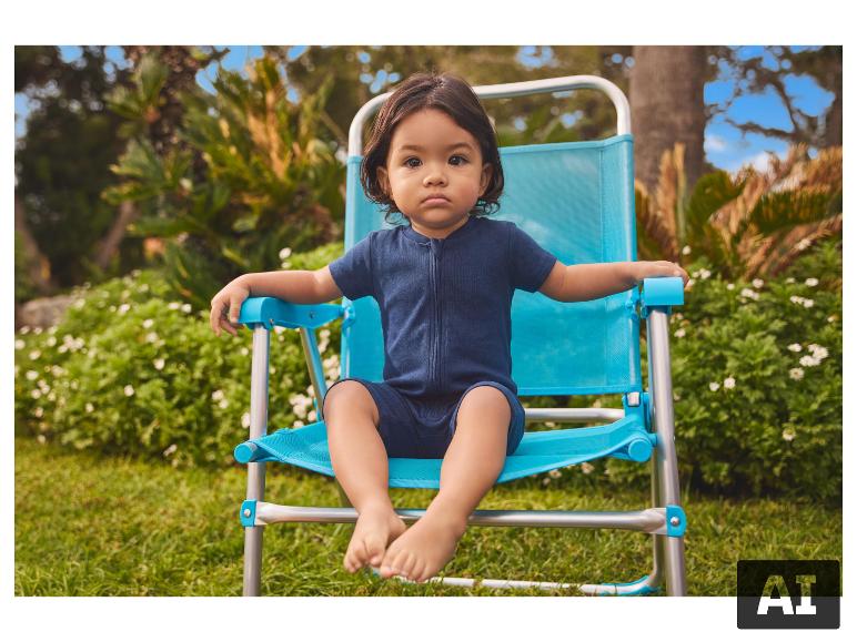 Bébé en barboteuse bleue assis sur une chaise de plage bleue et argentée en extérieur.