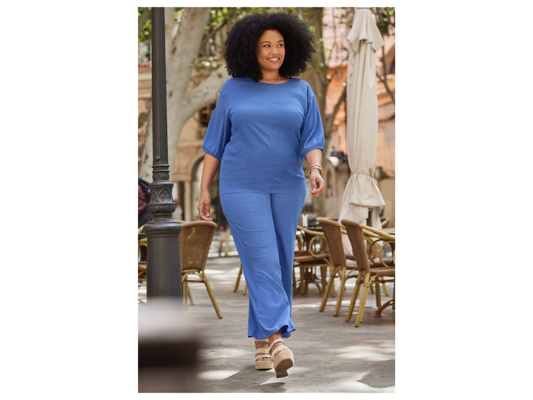 Une femme portant un pantalon et un haut bleus dans un environnement estival.