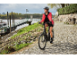 Femme à vélo électrique sur un chemin pavé au bord de la rivière.