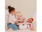 Fille jouant avec un ensemble de soins pour poupée rose, avec berceau et chaise haute.