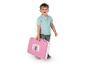 Un garçon souriant tient une valise rose sur le thème de Gabby's Dollhouse.