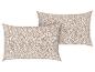 Deux oreillers beige à motifs floraux blancs.