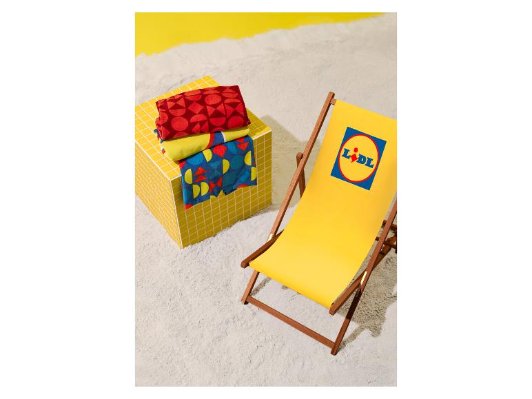 Chaise longue jaune avec logo et serviettes de plage à motifs sur un cube carrelé sur le sable.