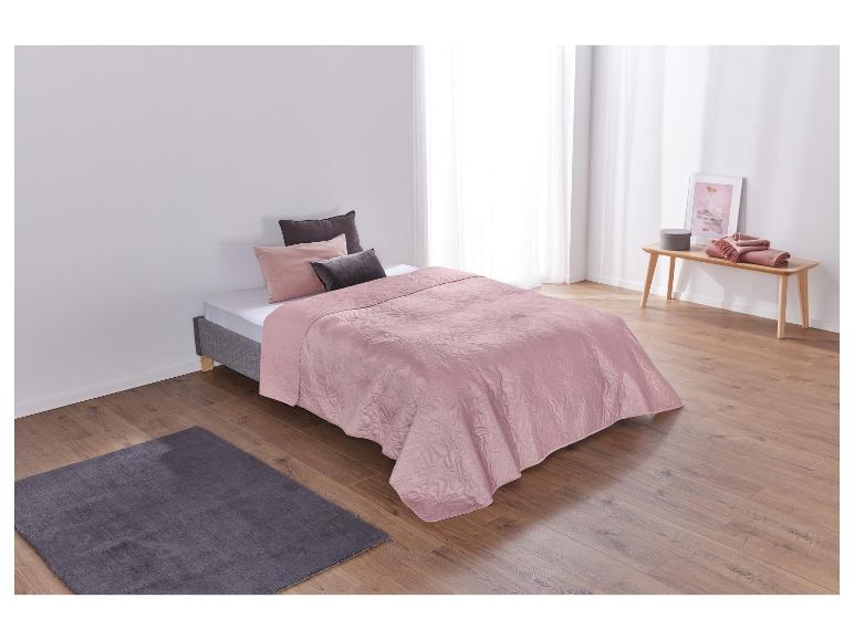 Chambre à coucher avec couvre-lit rose, oreillers foncés et parquet en bois.